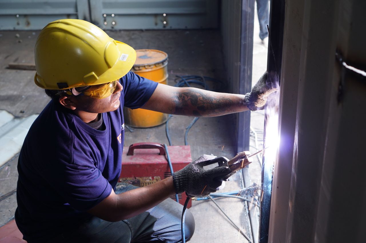 A professional welder working indoors with safety helmet and gloves, showcasing skill in metalwork.