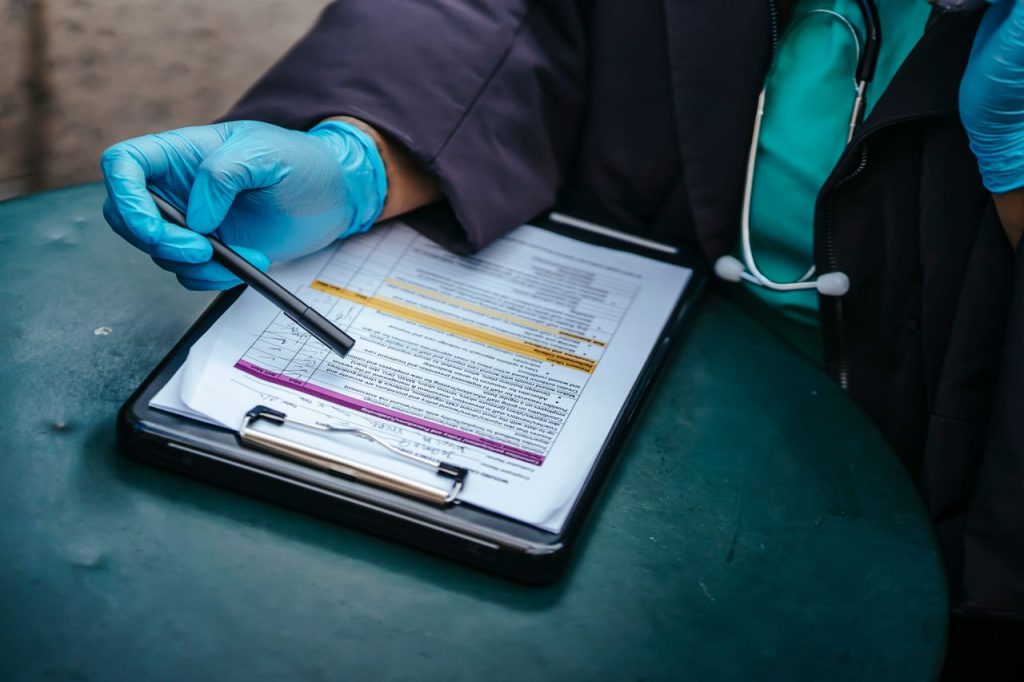 From above of crop anonymous plump female doctor in disposable gloves working at table with paper on clipboard